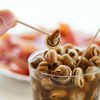 closeup of a man eating some caracolillos en caldo, a spanish recipe of small snails cooked and served in broth typical of andalusia, using a toothpick, on a table next to a plate with serrano ham